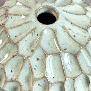 Pode incluir: Uma vista de perto de um vaso de cerâmica com um esmalte verde claro e um padrão texturizado em forma de favo de mel. O vaso tem uma abertura circular no topo e um acabamento brilhante. As bordas do padrão de favo de mel são marrons escuros.