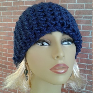 May include: A navy blue crocheted beanie hat with a slouchy fit. The hat is worn by a mannequin with blonde hair and earrings.