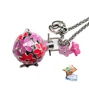 Puede incluir: Un collar de plata con un dije que es una bola redonda con flores rosas y rojas. El dije está unido a una cadena de plata con un pequeño dije de zapato de bebé de plata. El collar está sobre un fondo blanco.