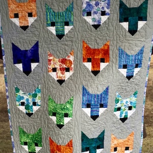 May include: A quilt with a gray background and a pattern of fox faces in various colors and patterns. The fox faces are arranged in a grid pattern.