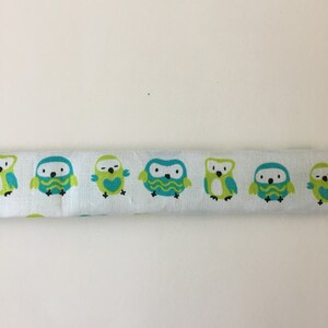 May include: A white fabric strip with a repeating pattern of green and blue owls. The owls have different facial expressions and designs.