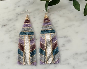 May include: A pair of long, beaded earrings with a geometric pattern in shades of purple, blue, white, and gold. The earrings have a fringe at the bottom.