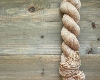 May include: A skein of beige yarn, tightly twisted into a rope-like form. The yarn is a light tan color, with subtle variations in tone. The yarn is displayed against a rustic wooden background.
