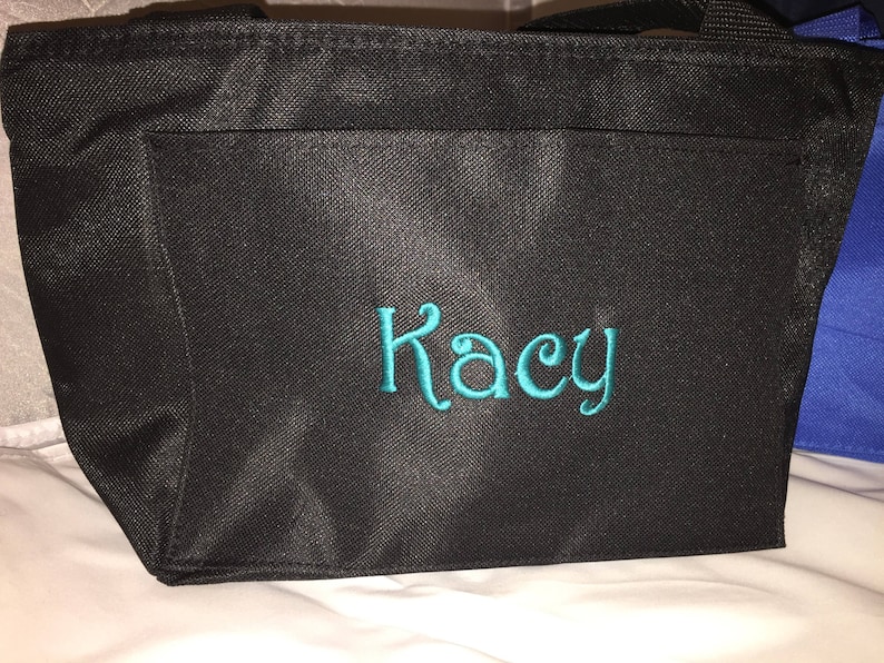 May include: Black insulated tote bag with a teal embroidered name "Kacy" on the front.