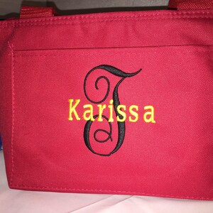 May include: Red tote bag with a black embroidered letter J and the name Karissa in yellow thread.