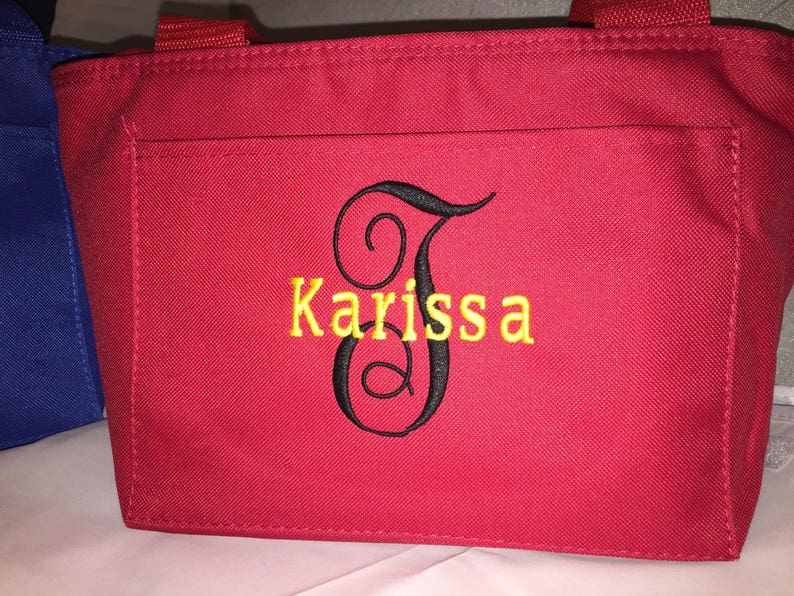 May include: Red tote bag with a black embroidered letter J and the name Karissa in yellow thread.