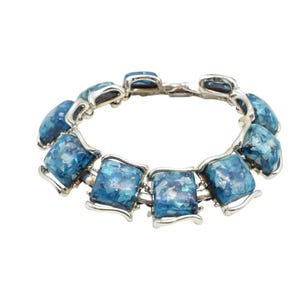 May include: A silver-tone link bracelet featuring a series of square-shaped, deep blue iridescent stone inlays. Each stone is set within a polished metal frame, connected by flexible silver-colored links to form a circular chain design.