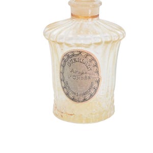 Pu&ograve; includere: Un flacone di profumo vintage con un design scanalato strutturato. La bottiglia &egrave; di colore giallo pallido e presenta un'etichetta con il testo "GUERLAIN Apr&egrave;s L'Ond&eacute;e". La bottiglia ha una parte superiore arrotondata e un piccolo tappo.