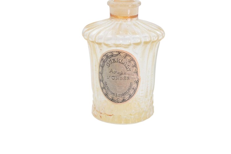 Pu&ograve; includere: Un flacone di profumo vintage con un design scanalato strutturato. La bottiglia &egrave; di colore giallo pallido e presenta un'etichetta con il testo "GUERLAIN Apr&egrave;s L'Ond&eacute;e". La bottiglia ha una parte superiore arrotondata e un piccolo tappo.