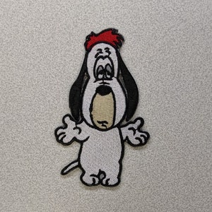 May include: An embroidered iron-on patch of a cartoon dog with a red hat, black ears, and white fur. The dog has a sad expression and is standing with its arms outstretched.