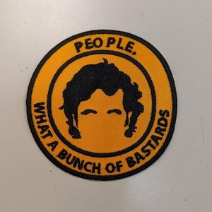 May include: A round, orange patch with black stitching and a black silhouette of a person's head with the text "PEOPLE. WHAT A BUNCH OF BASTARDS" around the edge.