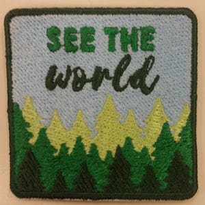 May include: A green and blue embroidered patch with a forest scene and the text "SEE THE world" in a cursive font.