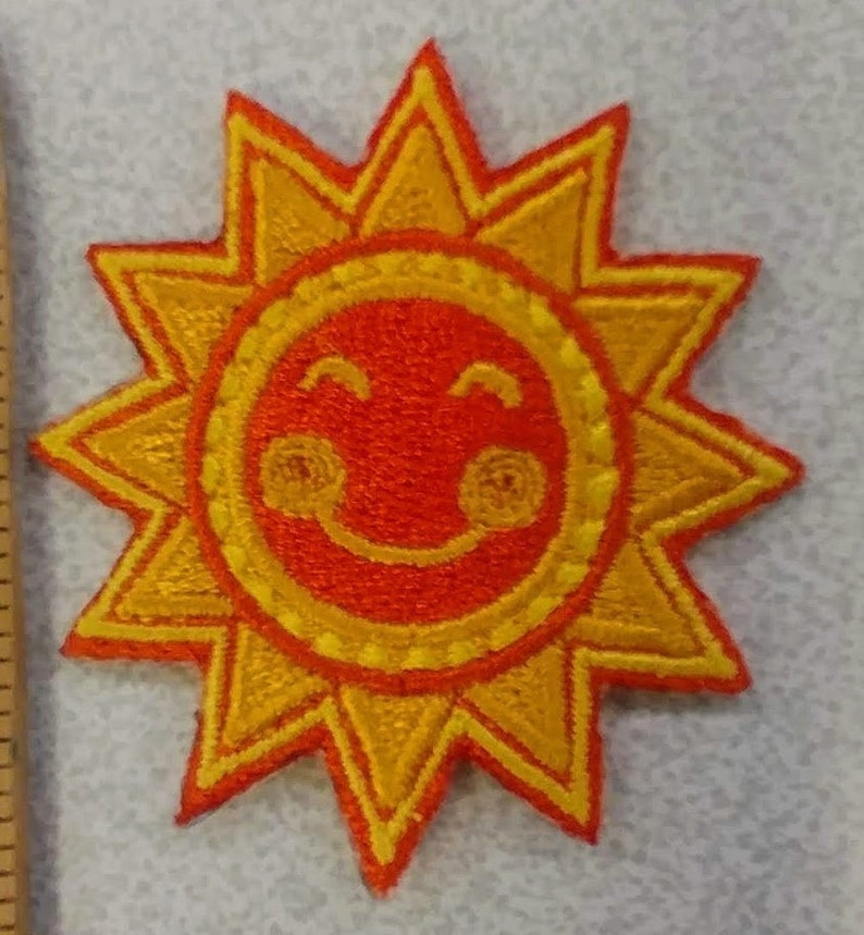May include: Embroidered patch featuring a smiling sun with a cheerful expression. The sun has a bright orange face and yellow rays, creating a vibrant and playful design. This patch is suitable for clothing, bags, or other fabric items.
