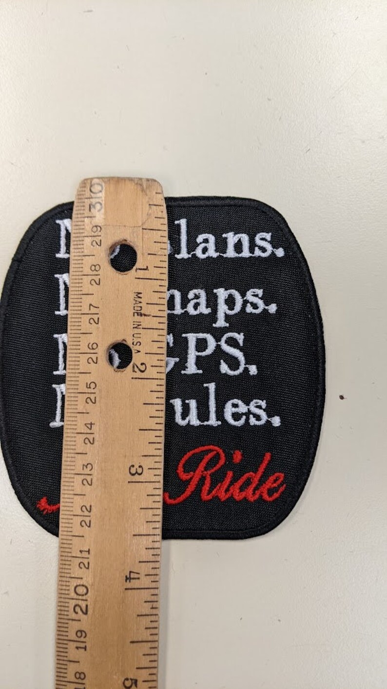 May include: Black and white embroidered patch with the text "No plans. No maps. PS. Rules. Ride" in white lettering. The word "Ride" is in red lettering. The patch is approximately 3 inches in diameter.