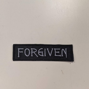 Puede incluir: Parche de tela negro con texto bordado en blanco que dice "FORGIVEN".