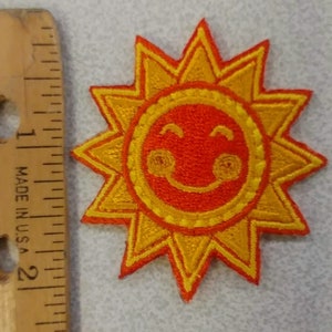 May include: Embroidered patch featuring a smiling sun design. The sun has a bright orange center with a yellow outline and rays. The patch is approximately 2 inches in diameter. The patch is made in the U.S.A.