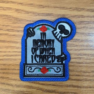 May include: An embroidered patch with a blue border, depicting a tombstone with a skull and the text "In memory of when I cared".