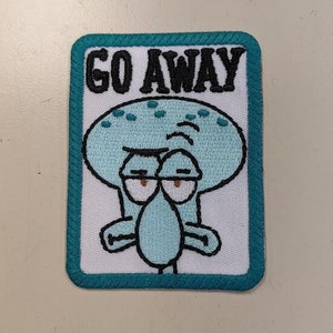 May include: An embroidered patch featuring a cartoon character with a blue face and the text "GO AWAY". The character has a grumpy expression and is surrounded by a teal border.