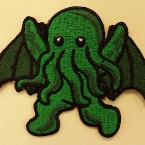 May include: Green embroidered patch of a cartoon Cthulhu with wings. The creature has large eyes and tentacles.