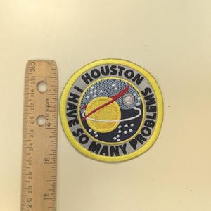 Puede incluir: Parche bordado circular con el texto "I HAVE SO MANY PROBLEMS" alrededor de un gr&aacute;fico de planeta. El parche tiene un borde amarillo. Una regla de madera est&aacute; al lado del parche. La regla est&aacute; marcada en cent&iacute;metros.