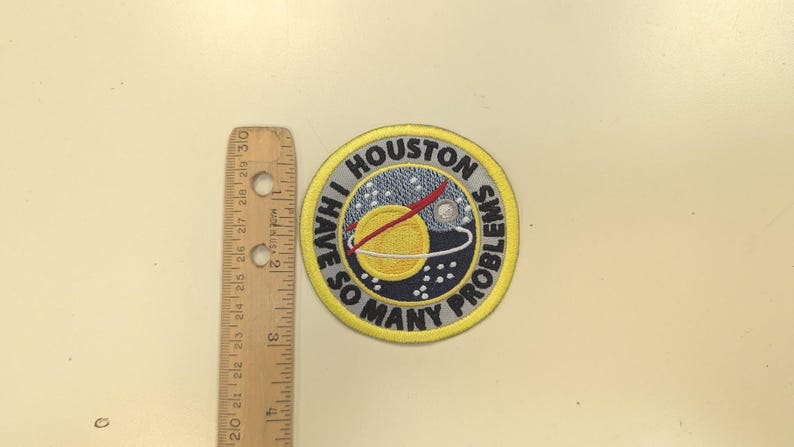 Puede incluir: Parche bordado circular con el texto "I HAVE SO MANY PROBLEMS" alrededor de un gr&aacute;fico de planeta. El parche tiene un borde amarillo. Una regla de madera est&aacute; al lado del parche. La regla est&aacute; marcada en cent&iacute;metros.