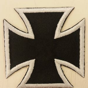 May include: Black iron cross patch with a white outline. The patch is made of fabric and has a stitched design.