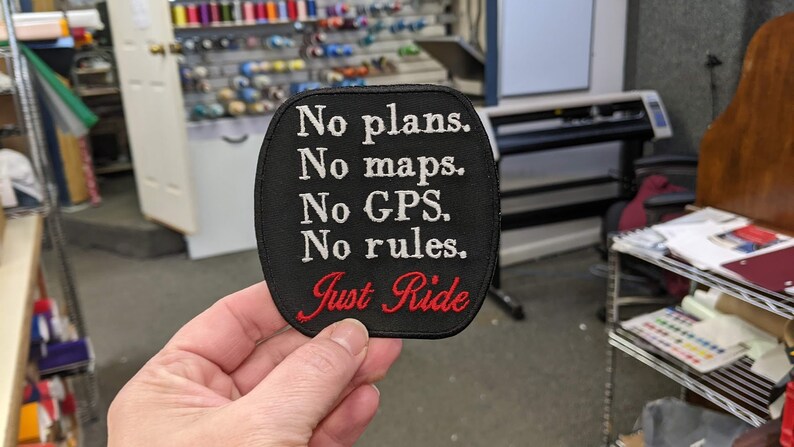 May include: Black embroidered patch with white text that reads "No plans. No maps. No GPS. No rules. Just Ride" in a red cursive font.