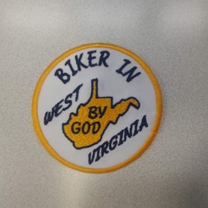 May include: A circular patch with a white background and a yellow border. The patch features the text "BIKER IN WEST BY GOD VIRGINIA" in navy blue, surrounding a yellow outline of West Virginia.