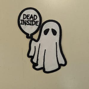 May include: White ghost patch with black outline and eye details, holding a speech bubble with the words "DEAD INSIDE" in black. The patch is likely for clothing or accessories.