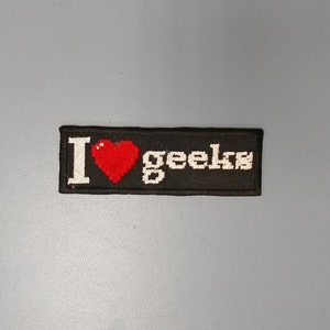 May include: Black embroidered patch with white text that reads "I love geeks" and a red pixelated heart.