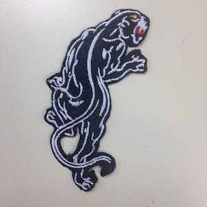 May include: Black and white embroidered iron-on patch of a panther with a red mouth and yellow eyes.