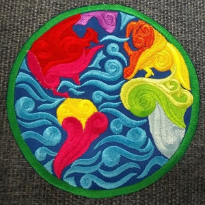 May include: A circular embroidered patch with a green border. The centre of the patch features a stylised design of the Earth with swirling blue, red, yellow, green, and pink colours.