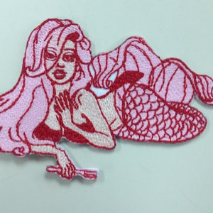 May include: Pink and red embroidered iron-on patch of a mermaid with long flowing hair holding a fork.