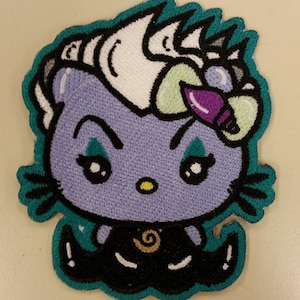 May include: An embroidered patch featuring a cartoon cat with a purple bow, teal eyes, and a black and white horned hairstyle. The cat is wearing a black dress with a gold swirl design and is outlined in teal.