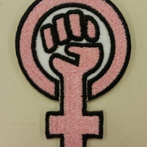 May include: Pink and black embroidered iron-on patch featuring a raised fist inside a circle with a female symbol below.