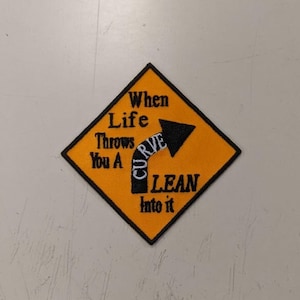 May include: Yellow diamond-shaped patch with black border and white text. The text reads "When Life Throws You A Curve Lean into it". A black arrow with a white curve is pointing to the right.