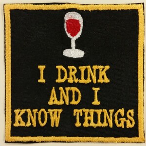 May include: A black and gold embroidered patch with a red wine glass and the text "I drink and I know things".