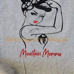 May include: Gray t-shirt with a black and white illustration of a woman with her fist raised in the air. The text "Mountain Momma" is printed in red below the illustration.