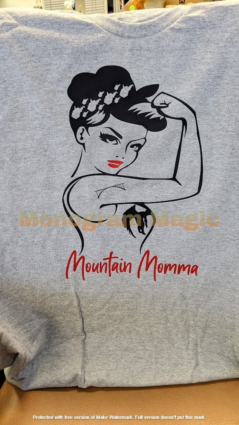 May include: Gray t-shirt with a black and white illustration of a woman with her fist raised in the air. The text "Mountain Momma" is printed in red below the illustration.