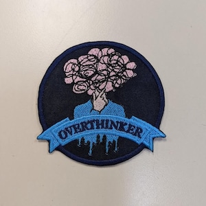May include: A blue and pink embroidered patch with a brain-shaped cloud over a person's head and the text "Overthinker" on a blue banner.