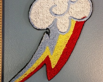 May include: An embroidered iron-on patch featuring a white cloud with a rainbow lightning bolt. The bolt is red, yellow, and blue.