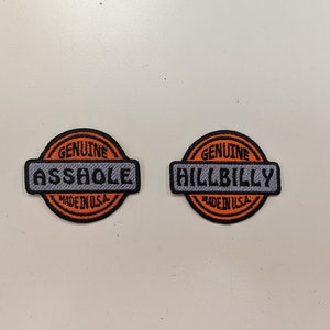 May include: Two embroidered patches with a circular design. One patch reads "GENUINE ASSHOLE" and the other reads "GENUINE HILLBILLY." Both patches have an orange border and the text "MADE IN U.S.A."