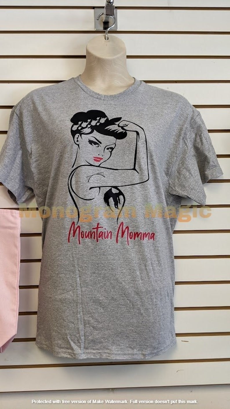 May include: Gray t-shirt with a black and white graphic of a woman with her arm raised and the text "Mountain Momma" in red.