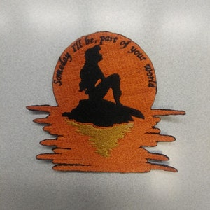 May include: An orange and black embroidered patch featuring a silhouette of Ariel from The Little Mermaid sitting on a rock with the words "Someday I'll be, part of your world" around her.