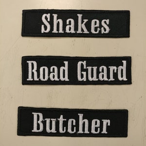 May include: Three black fabric patches with white embroidered text. The patches read "Shakes", "Road Guard", and "Butcher".