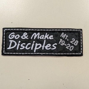 May include: Black rectangular patch with white stitched border. The patch features the embroidered text "Go & Make Disciples" and "Mt. 28 19-20" in white. The patch is on a light beige surface.