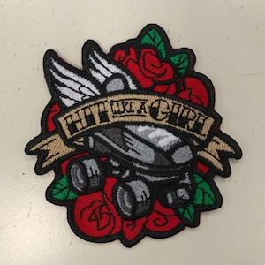 May include: Embroidered patch with a gray robot wearing a helmet and wings, surrounded by red roses and a banner that reads "Hit Like a Girl!"