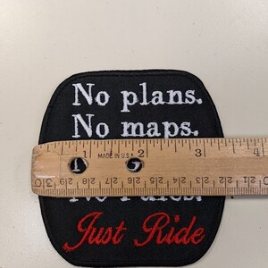 May include: Black embroidered patch with white text that reads "No plans. No maps. Just Ride" in a cursive font. The text "Just Ride" is in red.