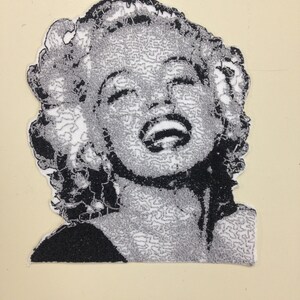 May include: Black and white embroidered patch of a woman with short, curly hair, smiling with her mouth open. The woman's hair is styled in a bouffant.