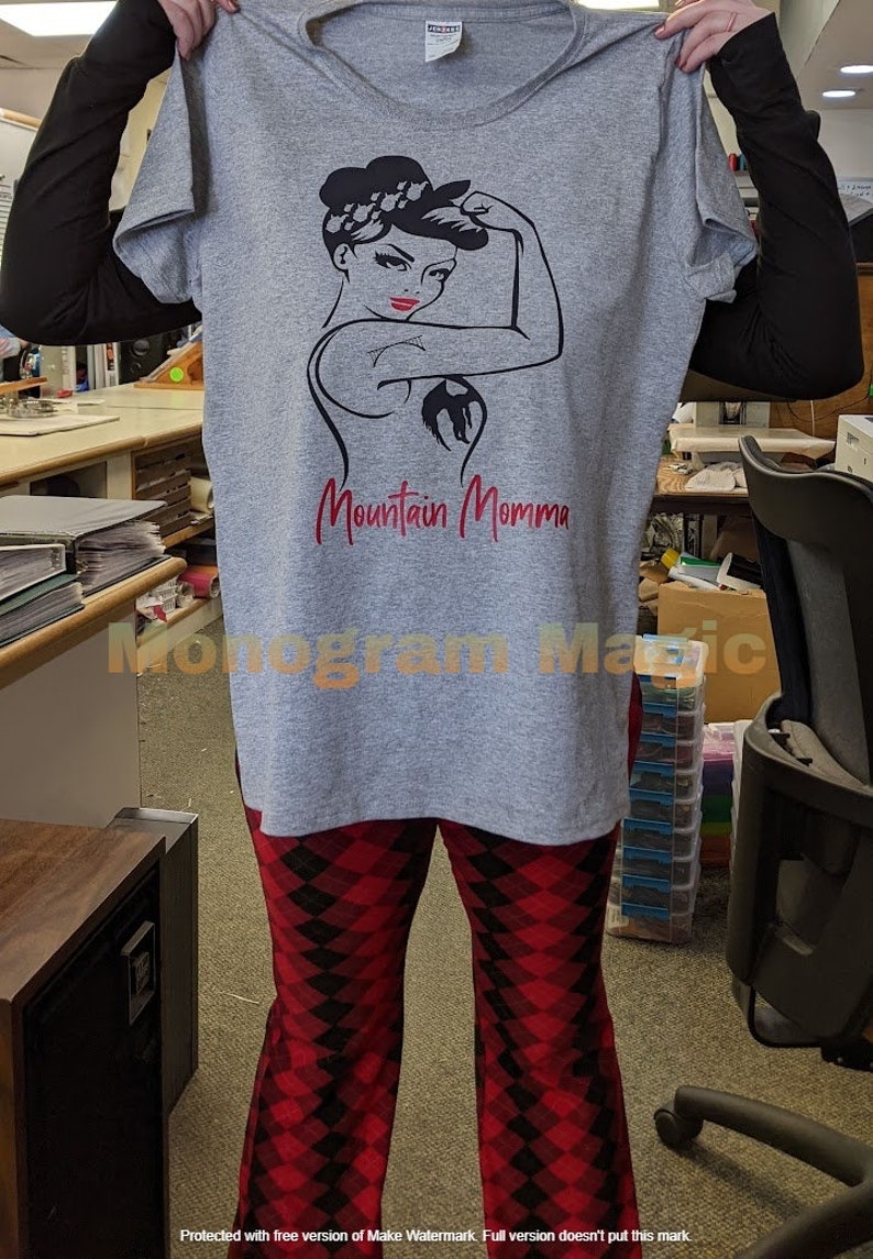 May include: Gray t-shirt with a black and white illustration of a woman with a red bandana and the text "Mountain Momma" in red.